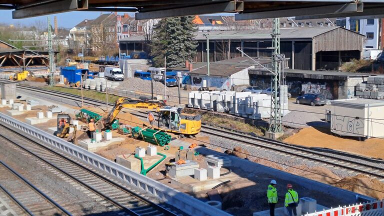 Baustelle an Bahngleisen mit Arbeitern und Baggern.