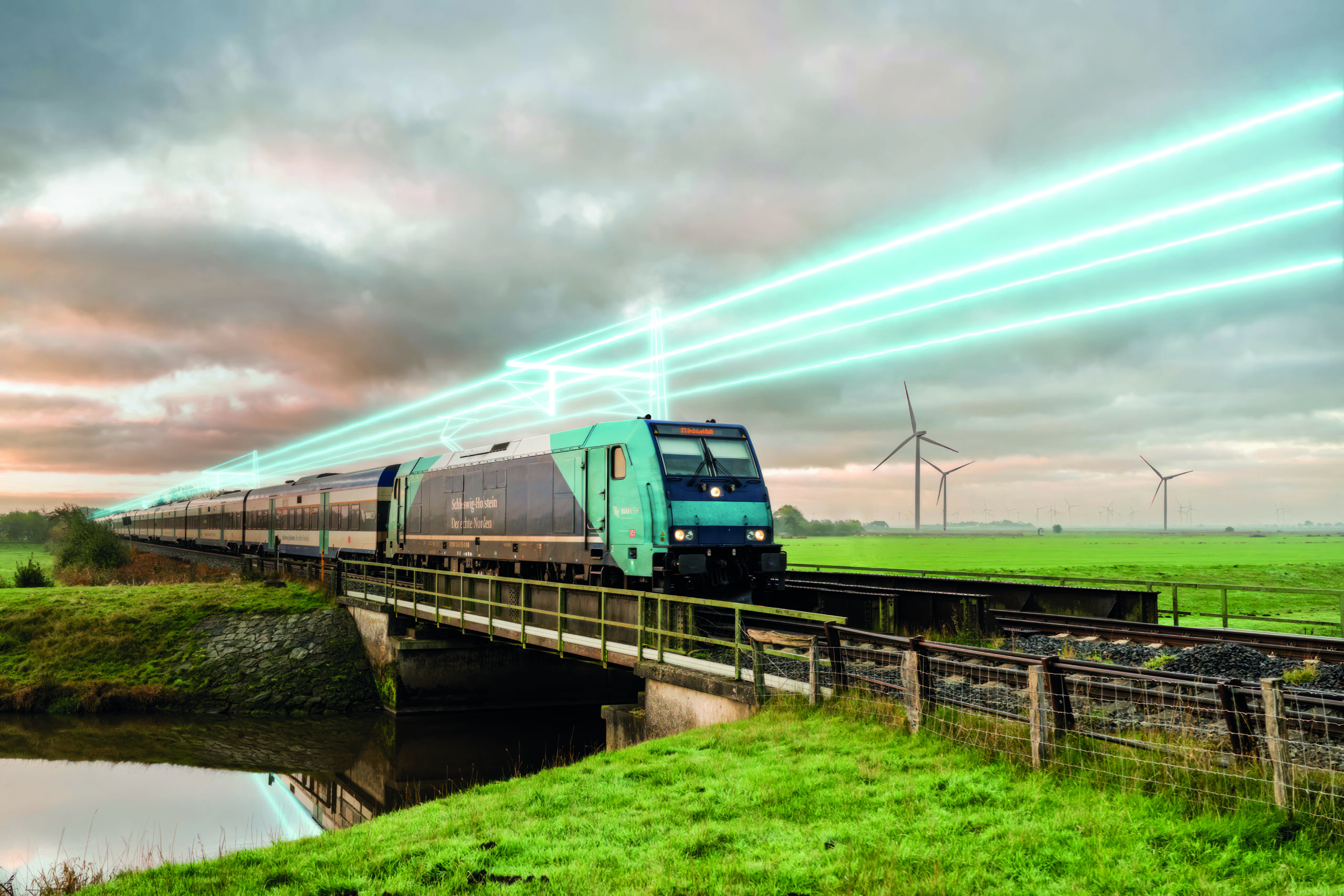 Zug auf der Marschbahn mit visualisierter Oberleitung in ländlicher Landschaft.